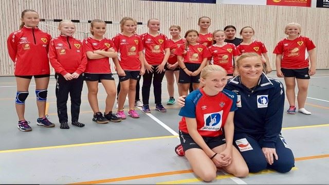 Maskot Maja med sin håndballjente, Emilie Christensen, og med Maja-laget i bakgrunnen. FOTO: B&Y Skjermbilde 2018-09-24 kl. 14.37.39.jpg